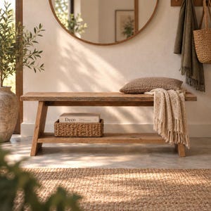 Peut inclure: Un banc rectangulaire en bois avec une étagère inférieure, comprenant un panier tressé marron texturé contenant un livre intitulé Deco, un coussin rectangulaire tressé marron et un plaid à franges couleur crème posé sur le côté du siège.