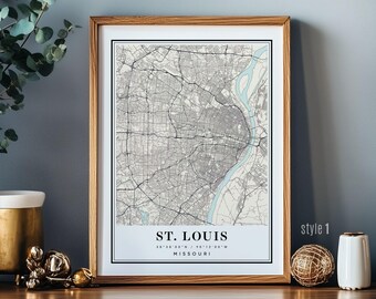 May include: Framed map print of St. Louis, Missouri, in grayscale. The map features city streets and the Mississippi River in light blue. The text "ST. LOUIS" and coordinates are at the bottom. The frame is light brown.