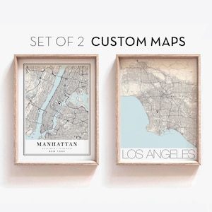 May include: Set of two custom maps in wooden frames. The map on the left shows Manhattan, New York City, with the text "Manhattan, New York" below the map. The map on the right shows Los Angeles, California, with the text "Los Angeles" below the map.