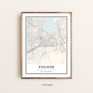 May include: A framed vintage map print of Folsom, California, with a light blue lake and beige background. The map includes street details and coordinates. The print is in a wooden frame with a white border and the word "vintage" at the bottom.