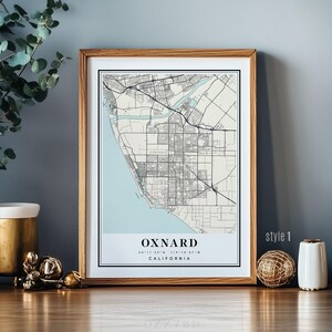 Może przedstawiać: Oprawiony wydruk mapy Oxnard, Kalifornia, w minimalistycznym stylu. Mapa przedstawia jasnoniebieski obszar przybrzeżny oraz szczegółowe odwzorowanie ulic i infrastruktury miasta. Wydruk oznaczony jest jako "style 1".