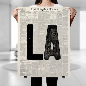 May include: A rectangular poster featuring a vintage Los Angeles Times newspaper page as the background. The letters LA are printed in large, bold, solid black ink over the center of the text, which includes columns of classified advertisements.