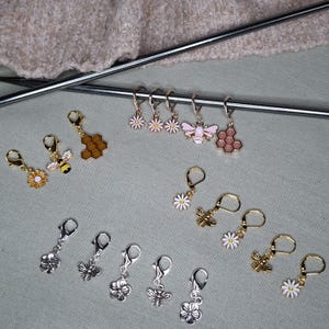 Könnte beinhalten: Ein Set mit 12 goldenen und silbernen Bienen- und Waben-Maschenmarkierern. Die Markierer zeigen verschiedene Designs, darunter Bienen, Waben und Blumen. Die Markierer sind perfekt, um beim Stricken oder Häkeln den Überblick über Ihre Maschen zu behalten.