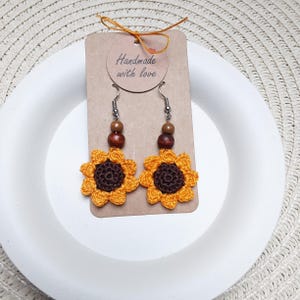 Op de afbeelding: Gehaakte zonnebloem oorbellen met bruine houten kralen en zilveren haakjes. De oorbellen zijn handgemaakt en worden geleverd met een kaartje waarop "Handmade with love" staat.