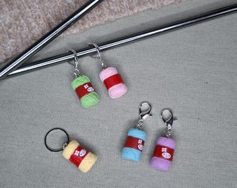 May include: A collection of colorful yarn-themed accessories, including earrings and a keychain. The earrings feature miniature yarn balls in green, pink, blue, and purple, each with a red band and silver hooks. The keychain has a yellow yarn ball with a red band.
