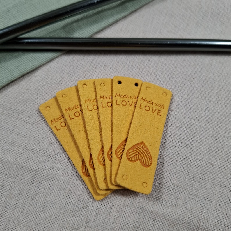 Op de afbeelding: Een waaier van zes mosterdgele rechthoekige labels met afgeronde hoeken. Elk label heeft een klein gaatje aan de bovenkant en de woorden "Made with LOVE" staan erop gedrukt. Een hartvormig ontwerp is in de onderkant van de labels ge&euml;mbosseerd.