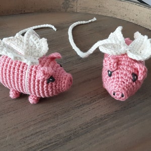 Puede incluir: Dos juguetes de cerdo de crochet rosa con alas de crochet blanco. Los cerdos tienen ojos y hocicos negros.
