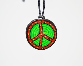 Puede incluir: Un collar con un colgante redondo en forma de signo de paz con un diseño de espiral verde y rojo. El colgante está hecho de arcilla y tiene un cordón negro.