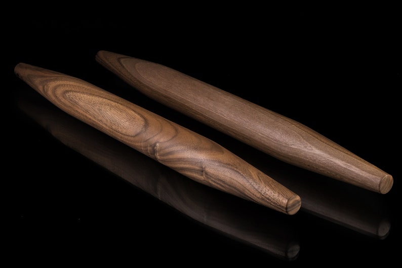 May include: Two wooden rolling pins, one longer than the other, with a dark brown wood grain pattern. The rolling pins are on a black surface.
