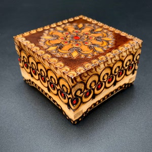 May include: A small wooden box with an intricate floral design carved into the top and sides. The design is in shades of brown and red.