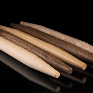 May include: Four wooden rolling pins of varying lengths and diameters, with a light brown, dark brown, and reddish brown wood grain. The rolling pins are arranged in a staggered pattern on a black surface.