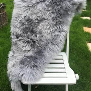 May include: A gray sheepskin rug draped over a white wooden chair. The rug is soft and fluffy, and the chair is simple and elegant.
