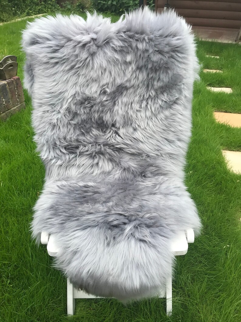 May include: A soft, gray sheepskin rug with long, fluffy fur. The rug is draped over a white folding chair and is sitting on a green grassy lawn.