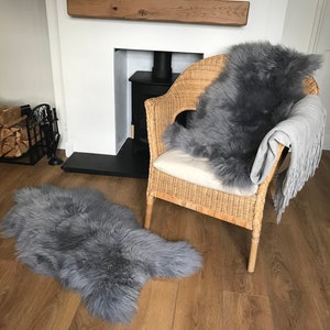 May include: Two gray sheepskin rugs, one on a wicker chair and one on the floor, in a living room with a fireplace.