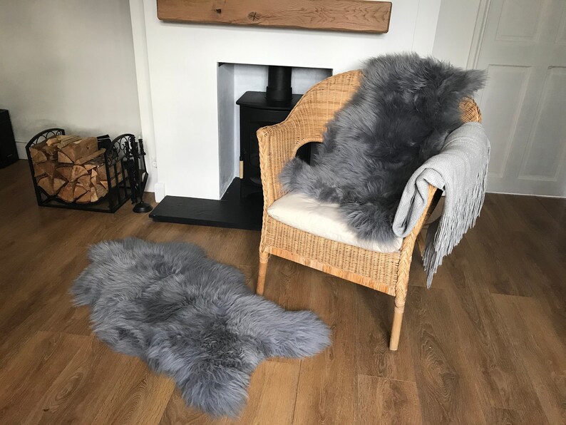 May include: Two gray sheepskin rugs, one on a wicker chair and one on the floor, in a living room with a fireplace.