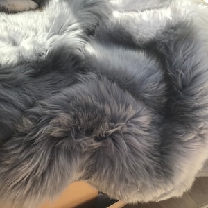 May include: A soft, gray faux fur rug with a fluffy texture. The rug is folded in half, showing the underside of the fur.