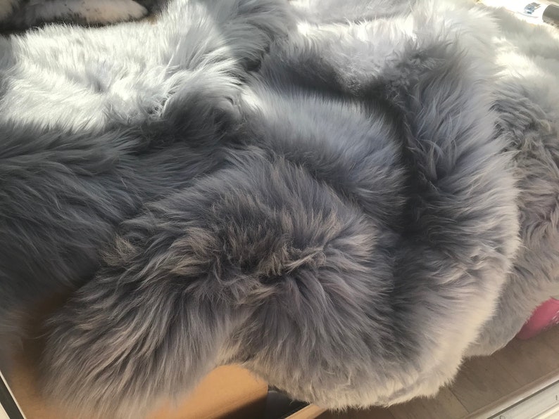 May include: A soft, gray faux fur rug with a fluffy texture. The rug is folded in half, showing the underside of the fur.