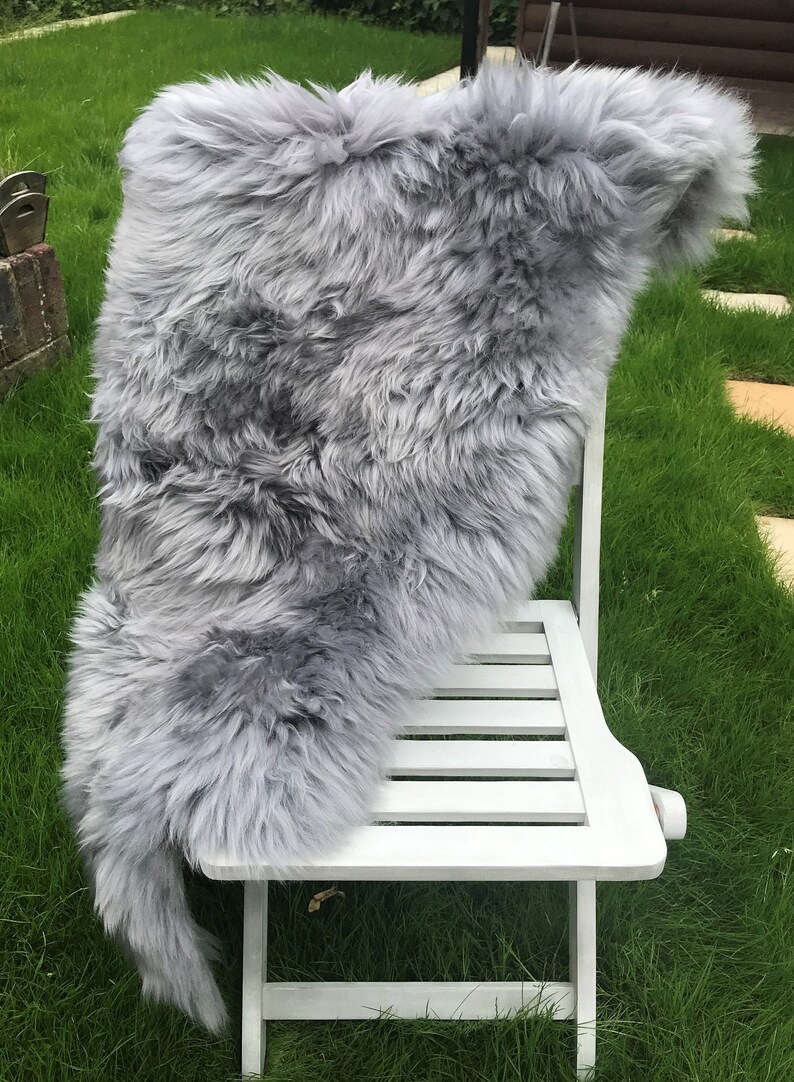 May include: A gray sheepskin rug draped over a white wooden chair. The rug is soft and fluffy, and the chair is simple and elegant.