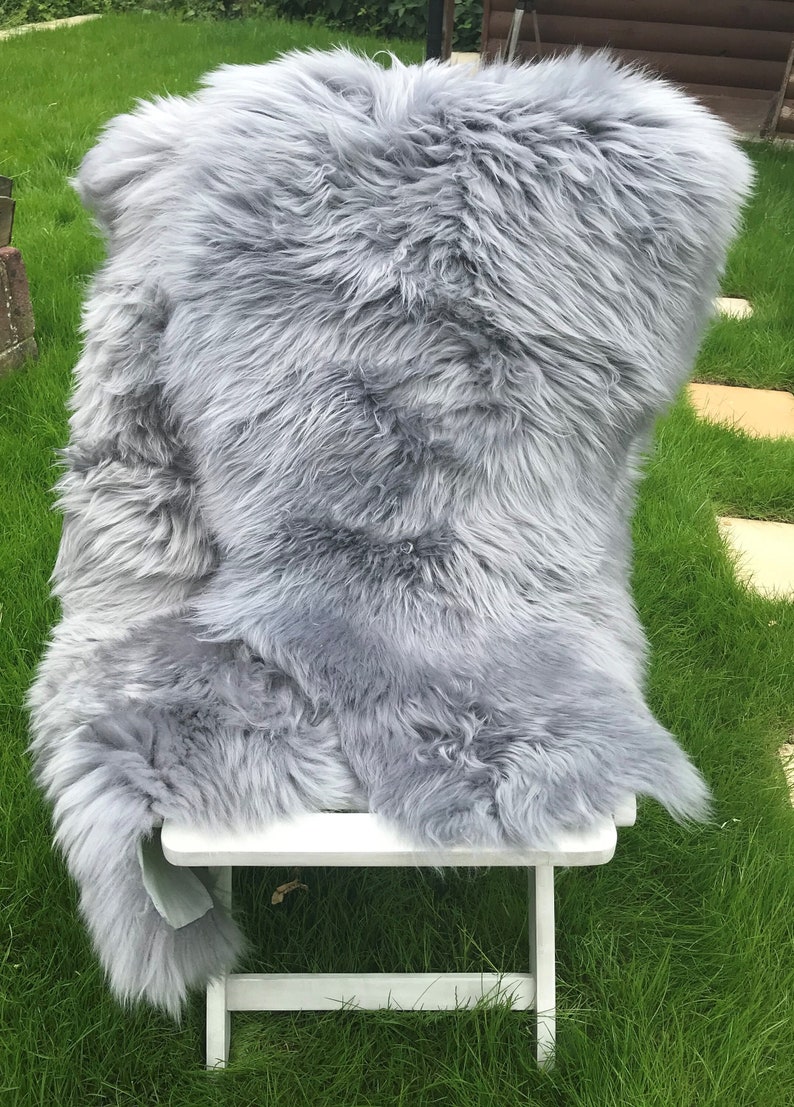 May include: A soft, gray sheepskin rug draped over a white folding chair. The rug is fluffy and has a natural, rustic look.