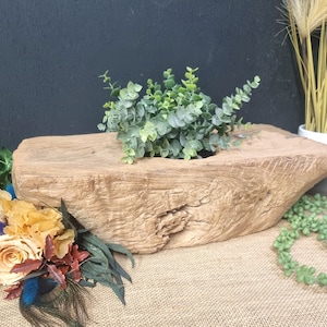 May include: A rustic wooden planter with a natural, weathered finish. The planter is filled with a lush green plant with small, rounded leaves. The planter is sitting on a hessian surface.