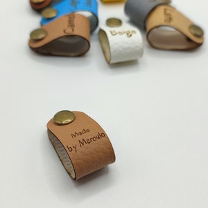Press fit riveted labels,no sew rivet tags,center fold labels with rivets,faux leather labels,faux leather tags,folding tags,rivet on labels