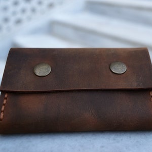 May include: A brown leather wallet with two metal snaps and a stitched edge.