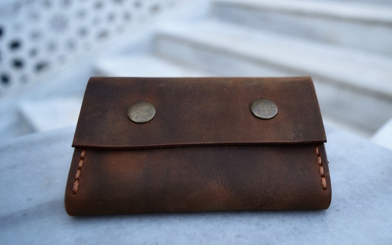 May include: A brown leather wallet with two metal snaps and a stitched edge.