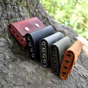 May include: Five leather key holders in different colors, including red, black, green, and brown. The key holders are stacked on top of each other and have multiple metal rings for attaching keys.