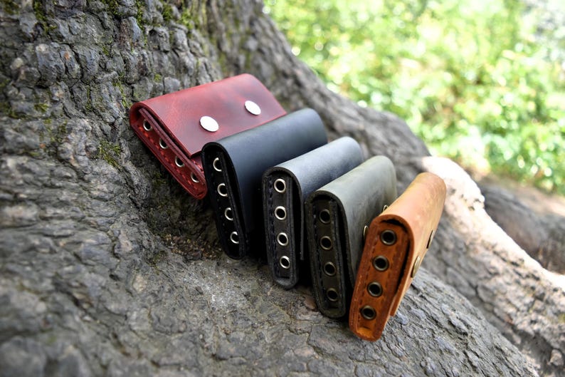 May include: Five leather key holders in different colors, including red, black, green, and brown. The key holders are stacked on top of each other and have multiple metal rings for attaching keys.