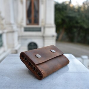 May include: A brown leather key holder with a distressed finish. It has two metal snaps and four key slots.