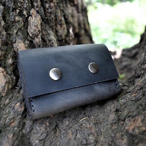May include: A black leather wallet with two silver snaps. The wallet is sitting on a tree trunk.