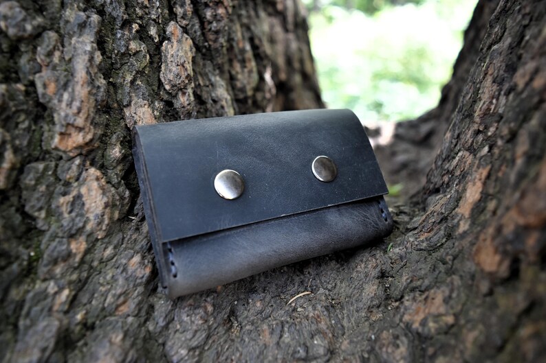 May include: A black leather wallet with two silver snaps. The wallet is sitting on a tree trunk.