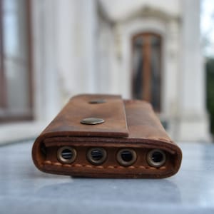 May include: A brown leather key holder with five key rings and two metal snaps. The key holder is on a white surface.