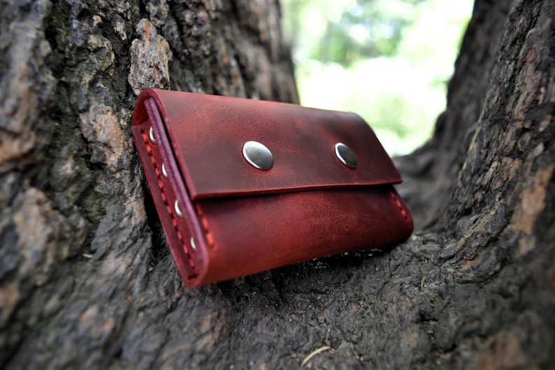 May include: A burgundy leather wallet with two silver snaps. The wallet is sitting on a tree trunk.