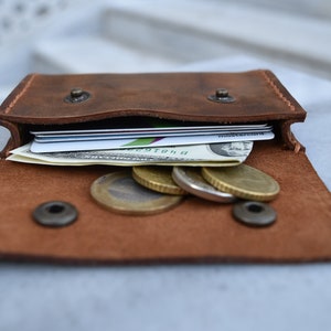 May include: A brown leather wallet with a flap open, revealing several credit cards, a dollar bill, and a few coins.