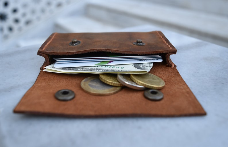 May include: A brown leather wallet with a flap open, revealing several credit cards, a dollar bill, and a few coins.