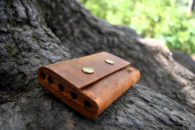 May include: A brown leather wallet with two brass snaps and multiple slots. The wallet is lying on a rough, textured surface.