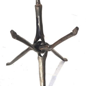 May include: A dark brown, handcrafted wooden tripod stand. The stand has a central vertical support with three legs extending outwards, and three additional legs extending upwards. The legs are connected at the centre.