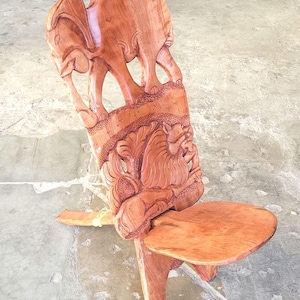 May include: A wooden folding chair carved with elephants and a lion. The chair is made of a reddish-brown wood and has a simple design.