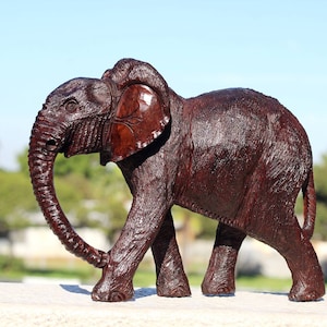May include: A dark brown wooden elephant figurine with a detailed carved design. The elephant is walking with its trunk curled up.