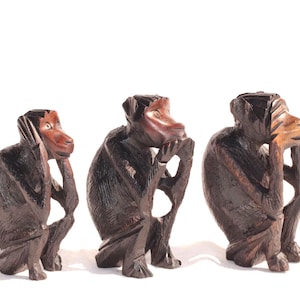 Puede incluir: Tres figuritas de mono de madera, cada una con un gesto diferente: una se tapa los ojos, otra se tapa las orejas y otra se tapa la boca. Los monos están tallados en madera marrón oscura y tienen rasgos realistas.