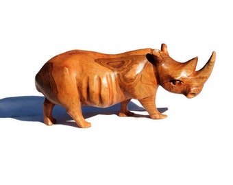 May include: A wooden carving of a rhinoceros, with a brown and reddish-brown color, standing on a white surface.