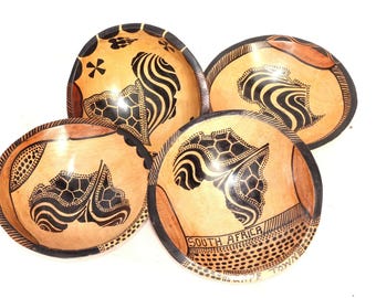 May include: Four wooden bowls with black and white geometric designs. The bowls are decorated with a stylized map of Africa and the text "South Africa".