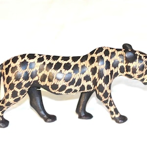 Op de afbeelding: Een zwart en gouden houten beeld van een lopende cheetah. De cheetah is gesneden met een gedetailleerd gevlekt patroon.