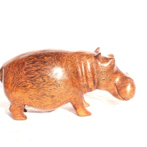 Puede incluir: Una escultura de madera de un hipopótamo, tallada en madera marrón oscura con un tono rojizo. La escultura está detallada con intrincados patrones de grano y un acabado liso.