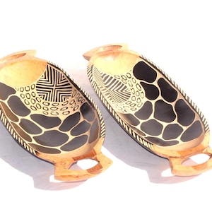 May include: Two wooden serving bowls with black and gold geometric patterns. The bowls have handles on each side.