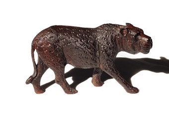 May include: A dark brown wooden sculpture of a leopard walking. The sculpture is detailed with spots and has a realistic appearance.