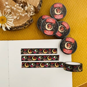 Op de afbeelding: Drie rollen zwarte en gouden washi tape met een herhalend patroon van rode paddenstoelen, halve manen en sterren. De tape is gelabeld met "Magic Mushrooms" en "Space Bird Crafts".
