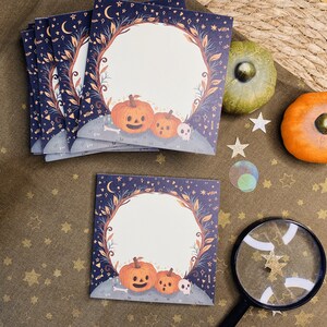 May include: A stack of square cards with a Halloween theme. Each card features a pumpkin illustration with a skull and a decorative border. The background is dark blue with stars and moons. There are also decorative pumpkins and stars.