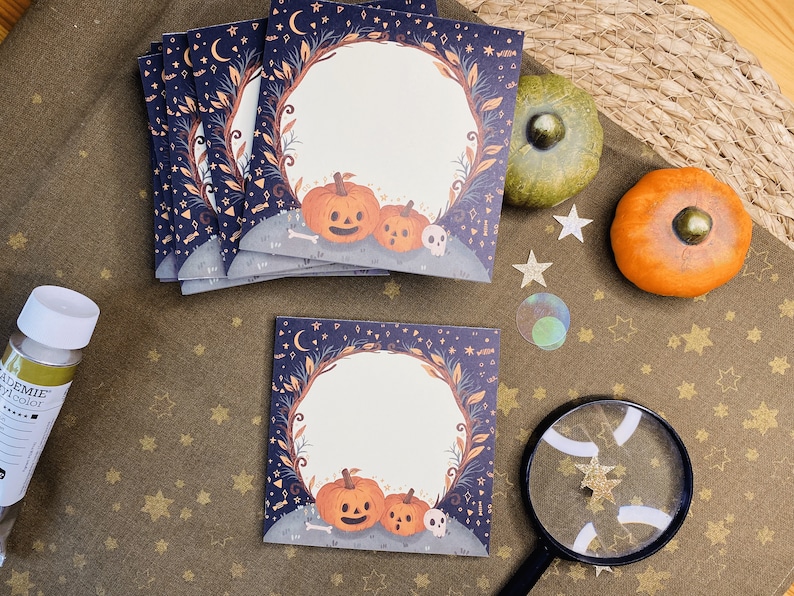 May include: A stack of square cards with a Halloween theme. Each card features a pumpkin illustration with a skull and a decorative border. The background is dark blue with stars and moons. There are also decorative pumpkins and stars.